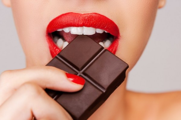 Indulging in a sweet affair with chocolate. Close-up of a beautiful women holding finger on her red lips while standing against grey background
