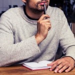 Man in kitchen is thinking and writing