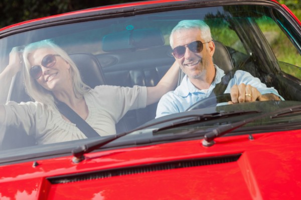 Happy mature couple in red cabriolet going for a ride on sunny day