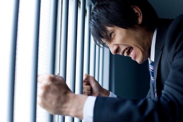 Businessman holding bars of cage and shouting