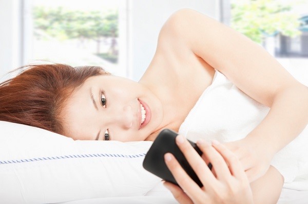 smiling young woman texting by smart phone on the bed