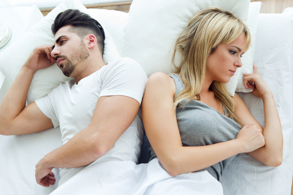 Upset couple lying back to back in bed