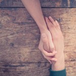 Close up on a man and a woman holding hands at a wooden table