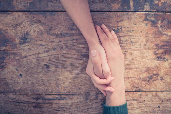 Close up on a man and a woman holding hands at a wooden table