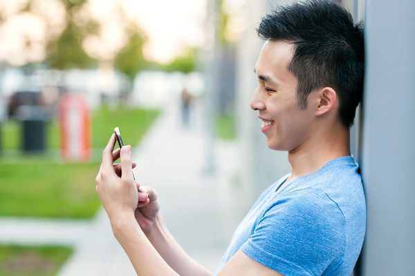 Young asian man smiling and looking at smart phone on city sidewalk