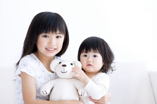 Girl holding her baby sister and a teddy bear