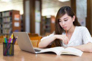 Asian beautiful female student study in library with laptop