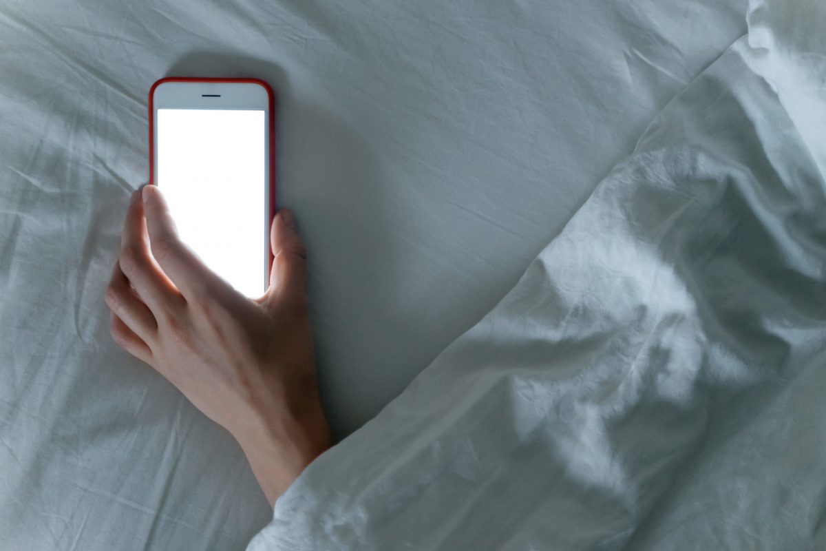 Smartphone laying in hand of sleeping female under blanket.